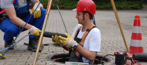 Mann mit rotem Helm und Arbeitskleidung steht in Abwasserschacht